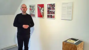 Ein Mann steht vor einer Wand an der Beispiele der Ausstellung zu sehen sind. Auf einem Sockel liegt ein Ansichtsexemplar einer Graphic Novel.