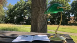 Eine Lampe steht auf einem Tisch vor einem Baum im Grünen, mit einer Zeitschrift auf dem Tisch